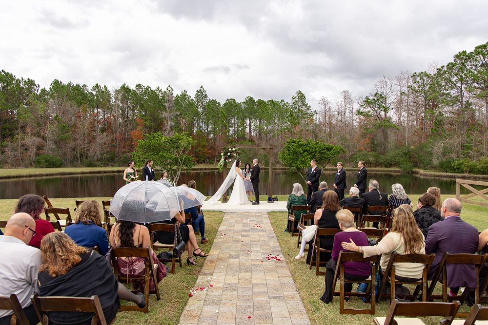 Guests seated at outdoor tables during a rustic wedding ceremony in a natural wooded setting.