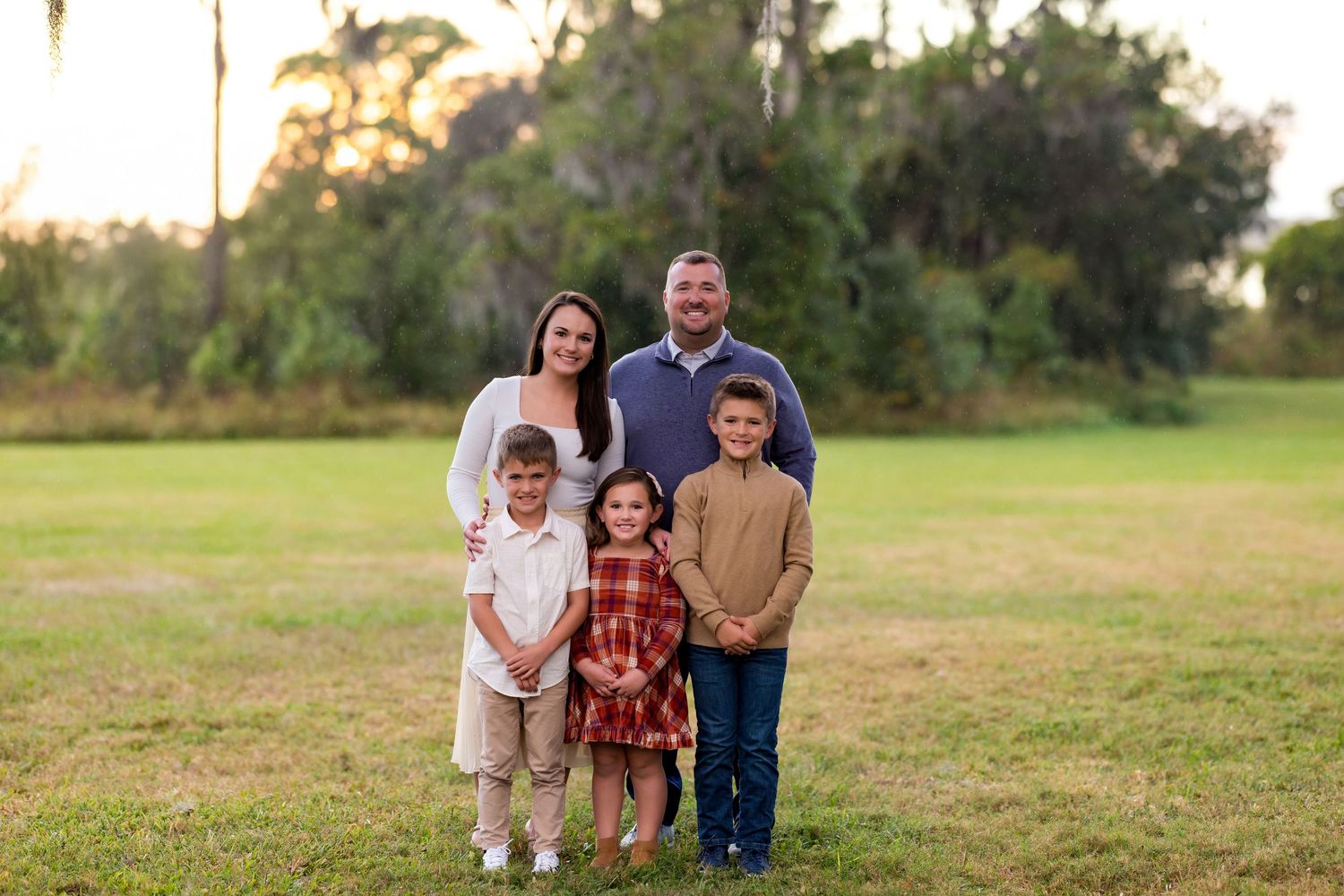 Family standing together in a grassy field at sunset during an outdoor photo session.