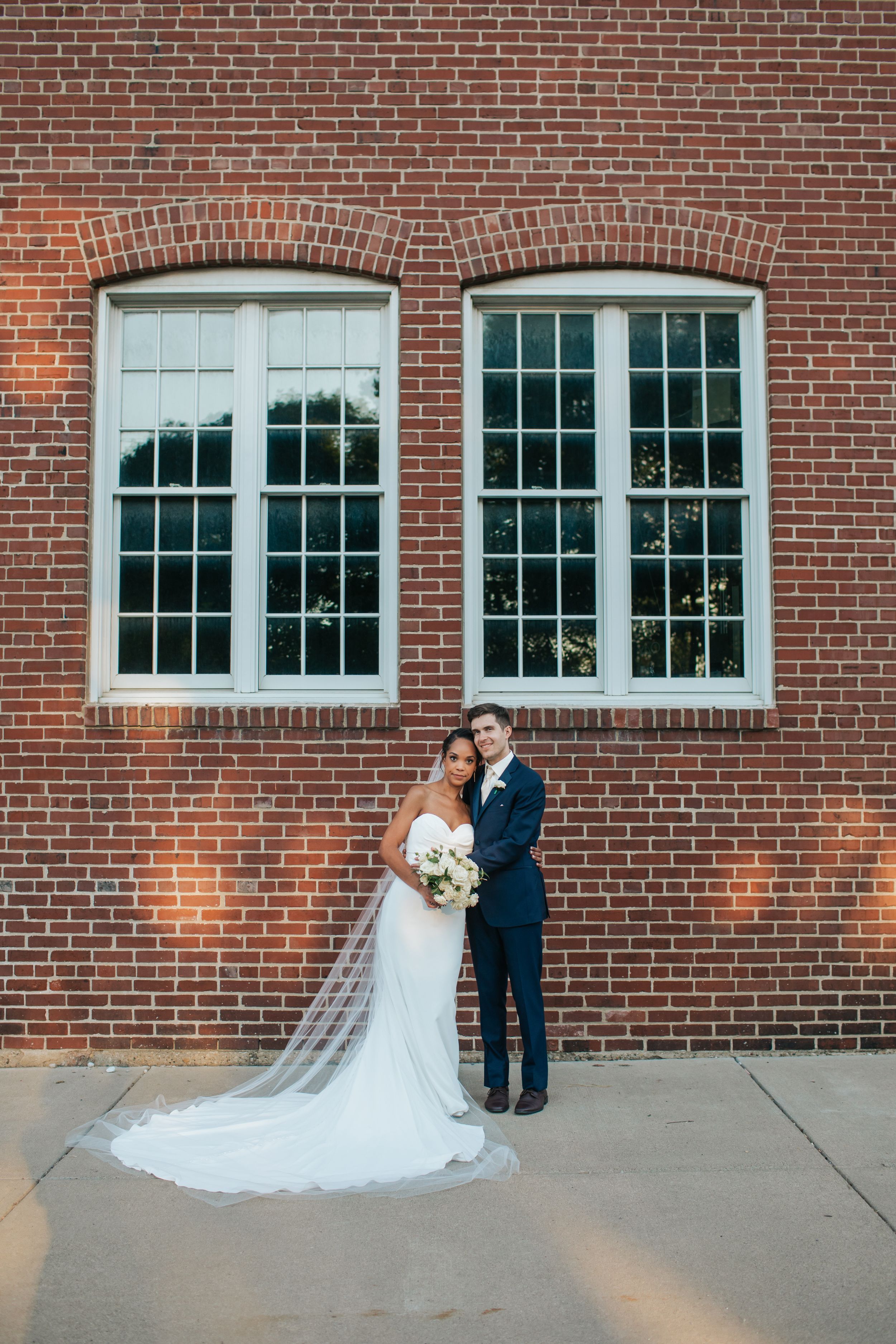 A couple shares a romantic moment against a rustic brick wall backdrop during their wedding celebration.