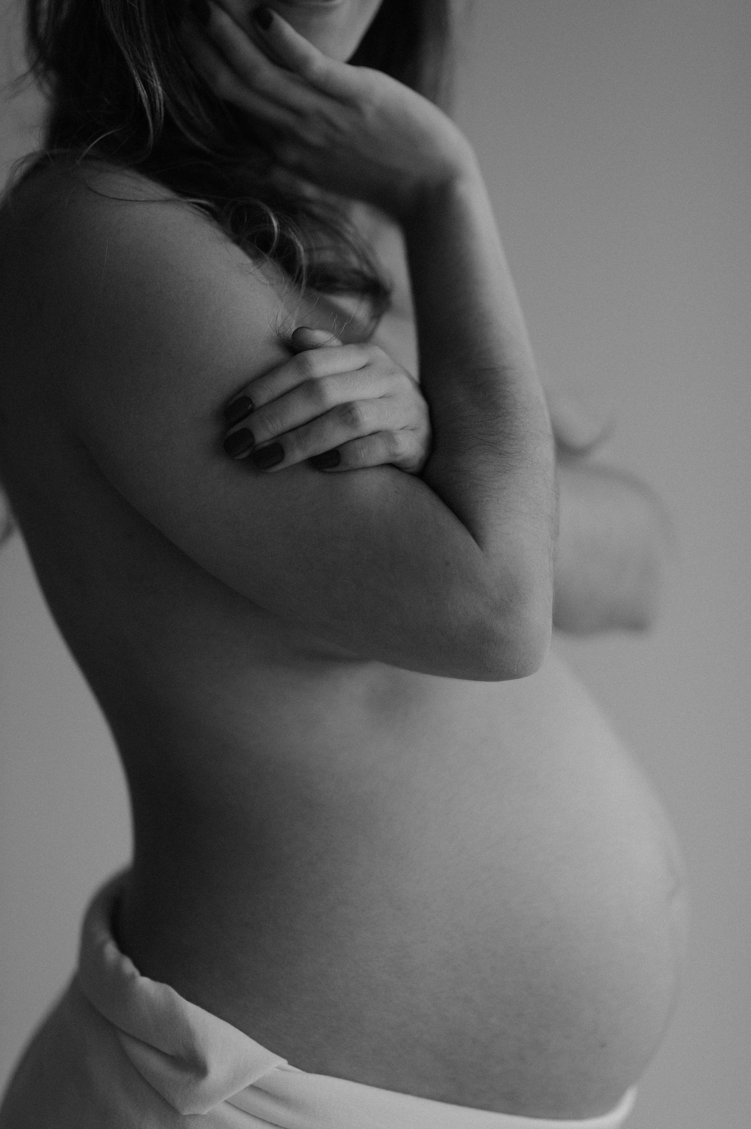 Black and white artistic photograph of a pregnant woman's bare belly and torso in soft natural light.