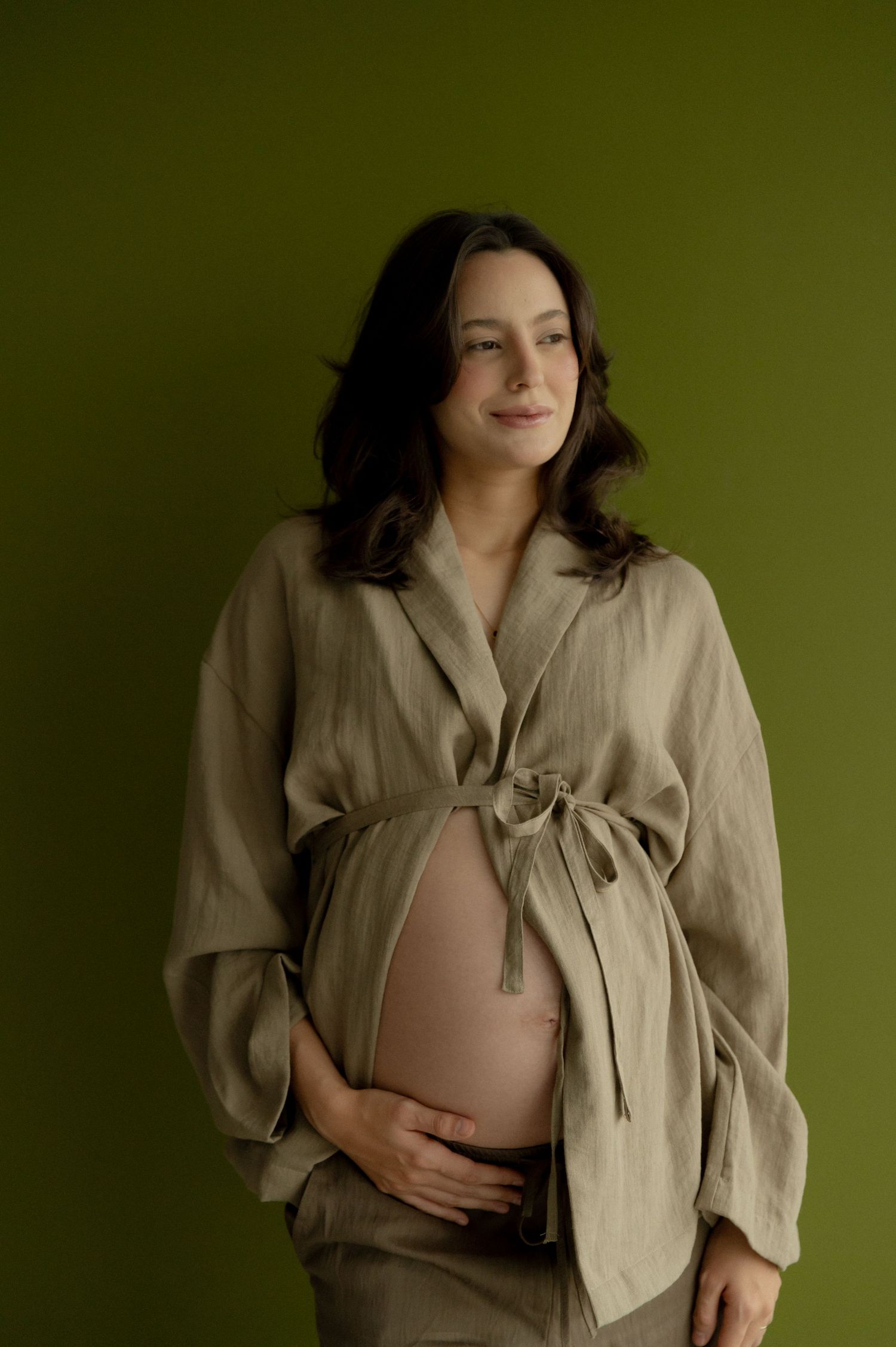 Artistic maternity photo series showing a pregnant woman in beige wrap top against dark green background.