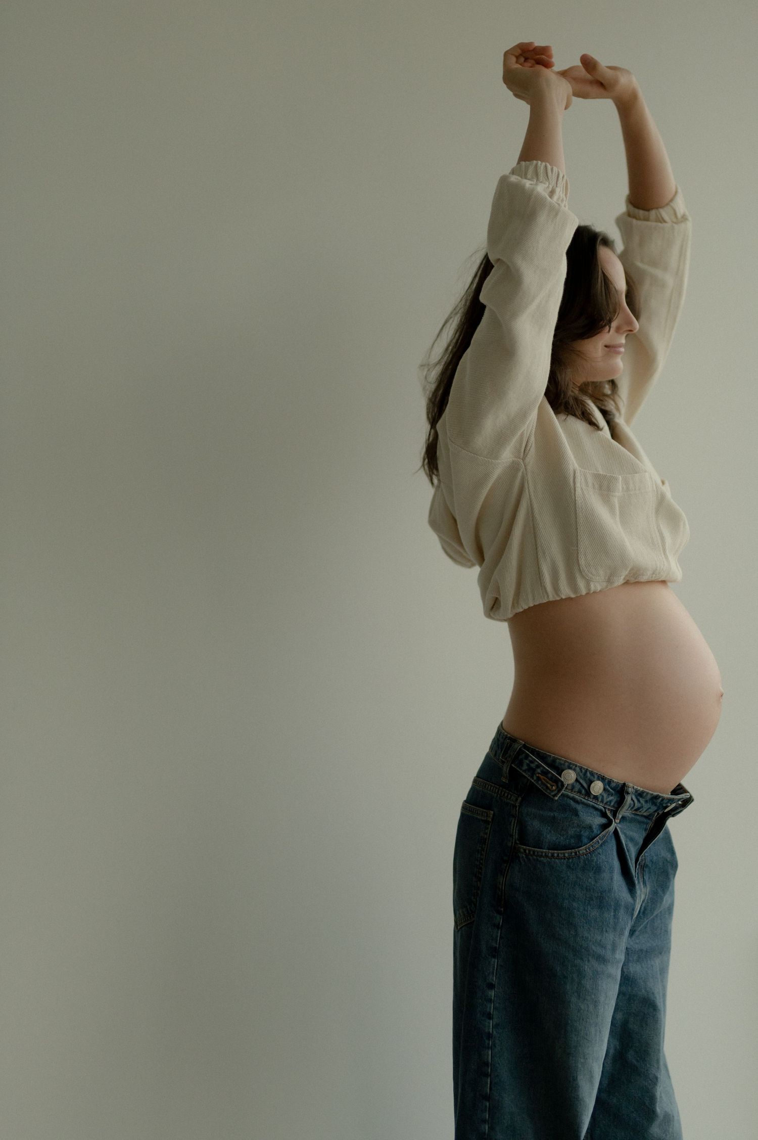 A series of artistic maternity photos showing a pregnant woman in jeans and white top against a light background.