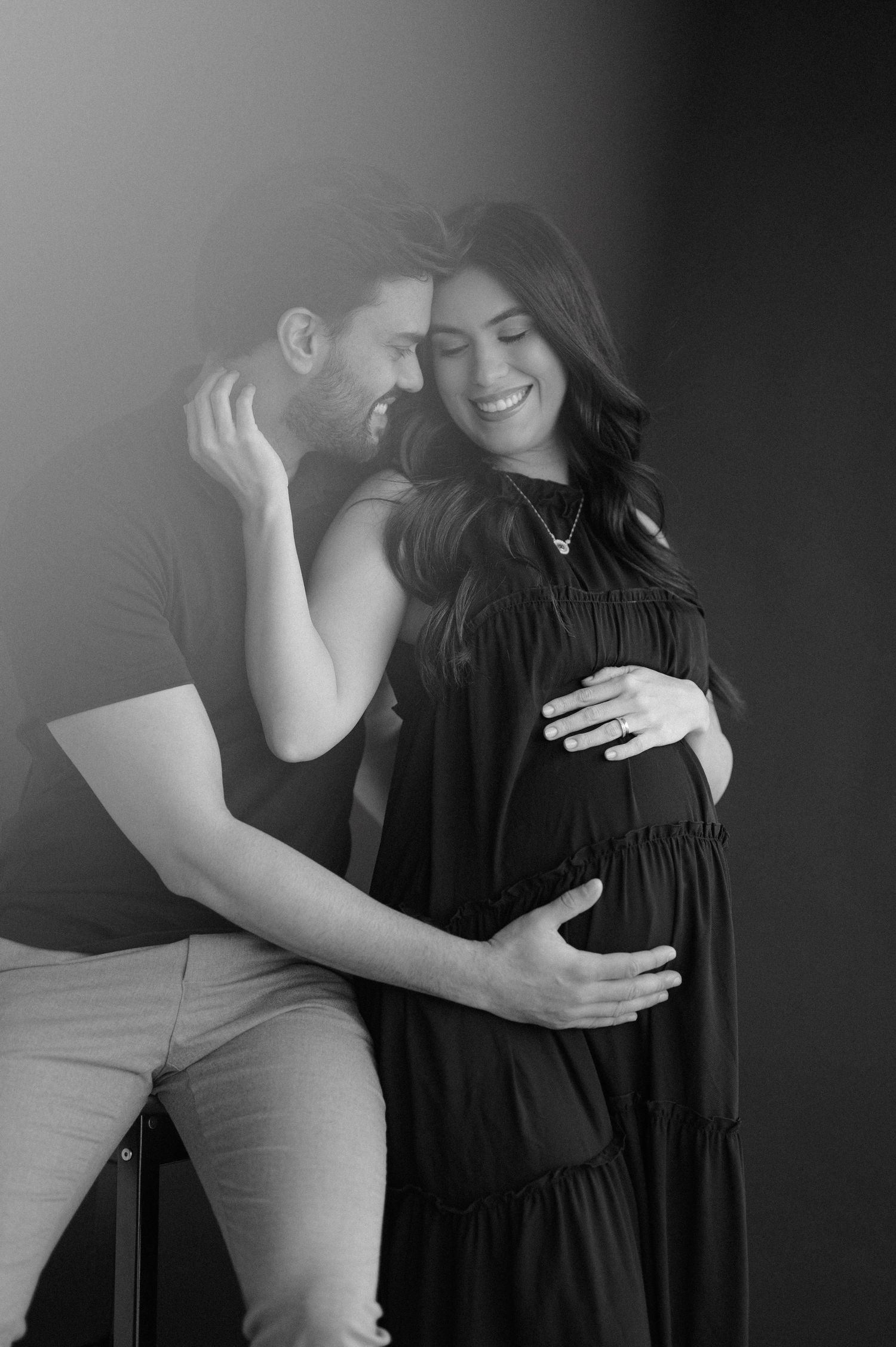 Black and white intimate maternity photo of couple sharing tender moment in studio setting.