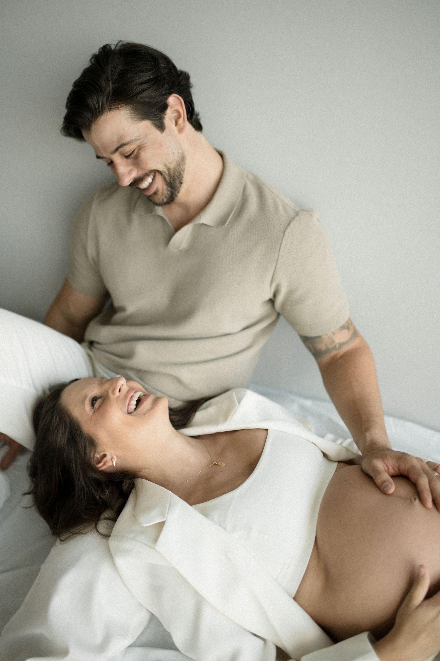 A couple shares a joyful intimate moment together while relaxing on white bedding.
