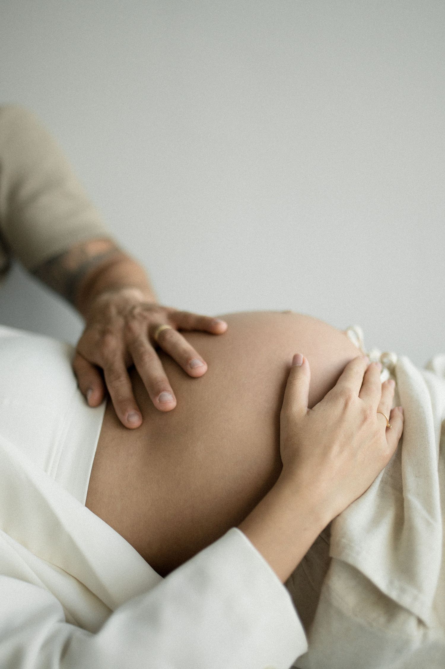 Two hands tenderly touching a pregnant belly against a light background.