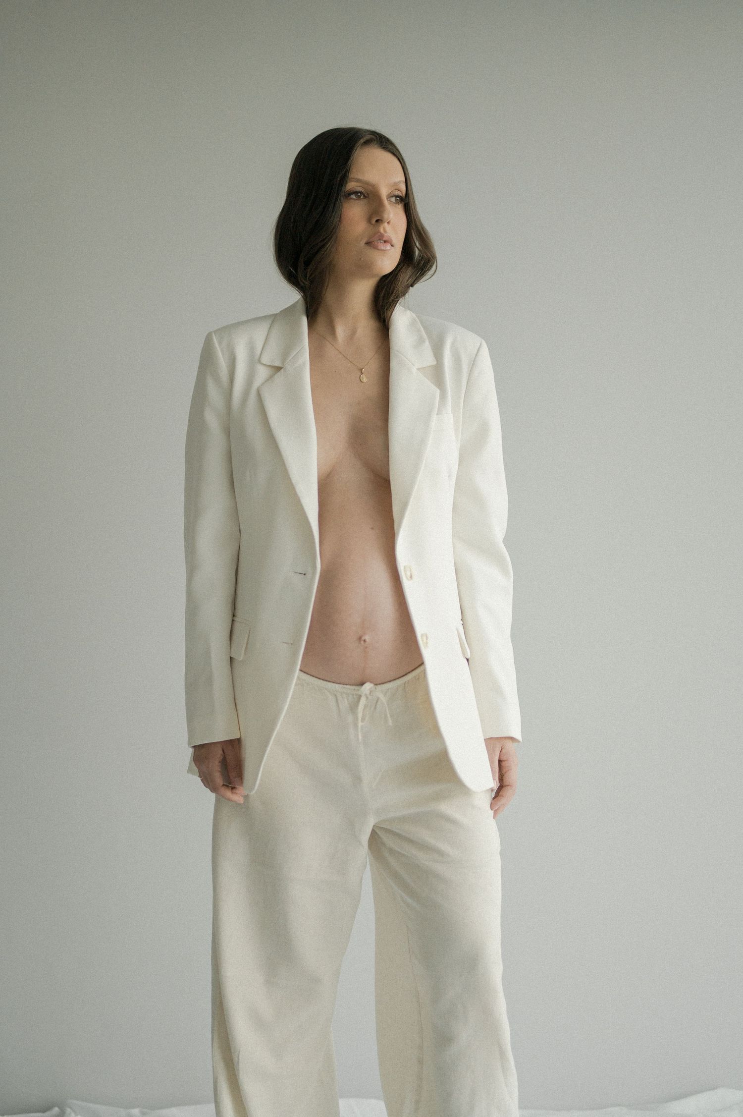 Person in white suit standing against neutral wall in minimalist fashion pose.