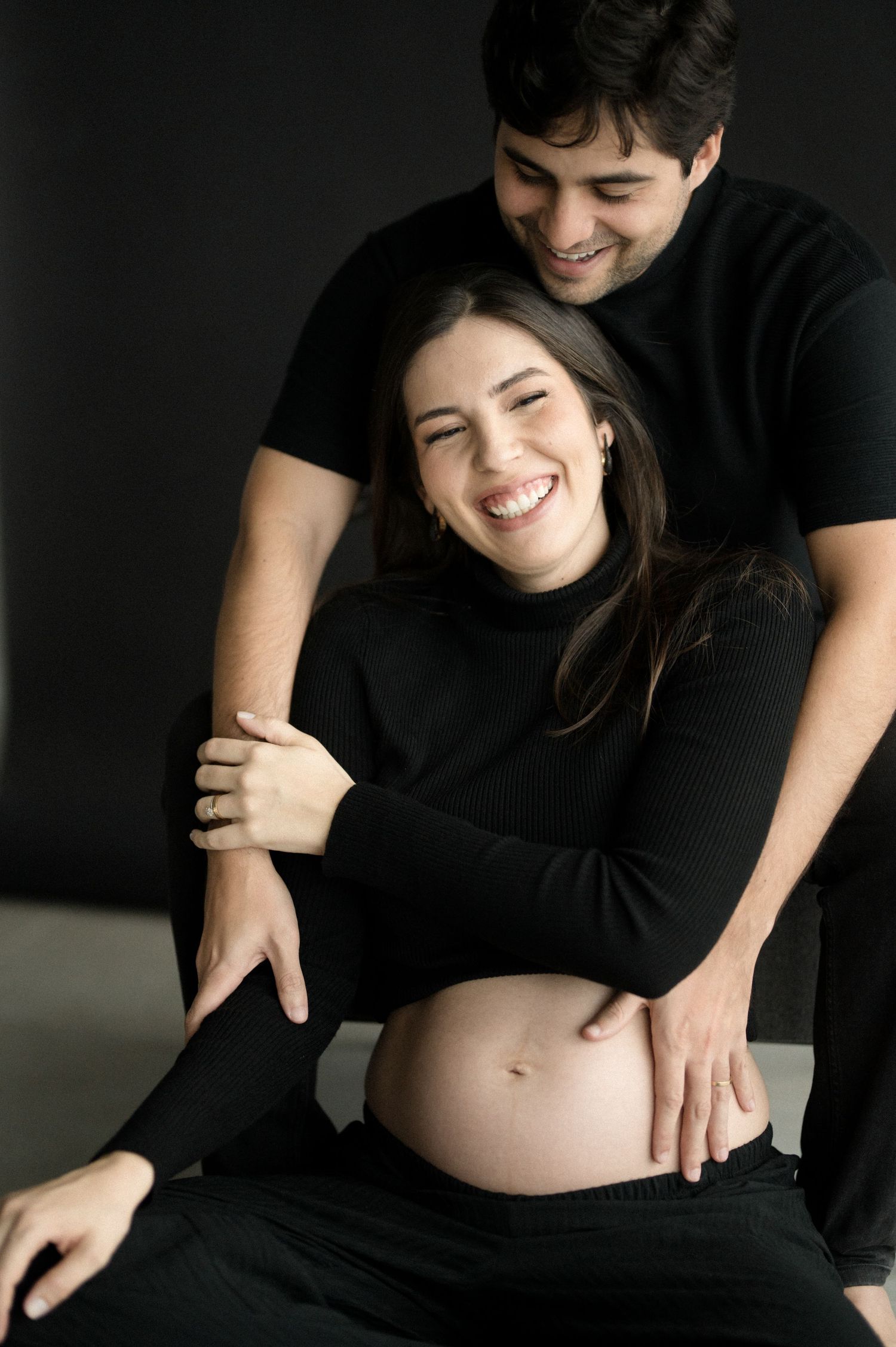 A series of intimate maternity photos showing a pregnant woman in black clothing against a dark background.