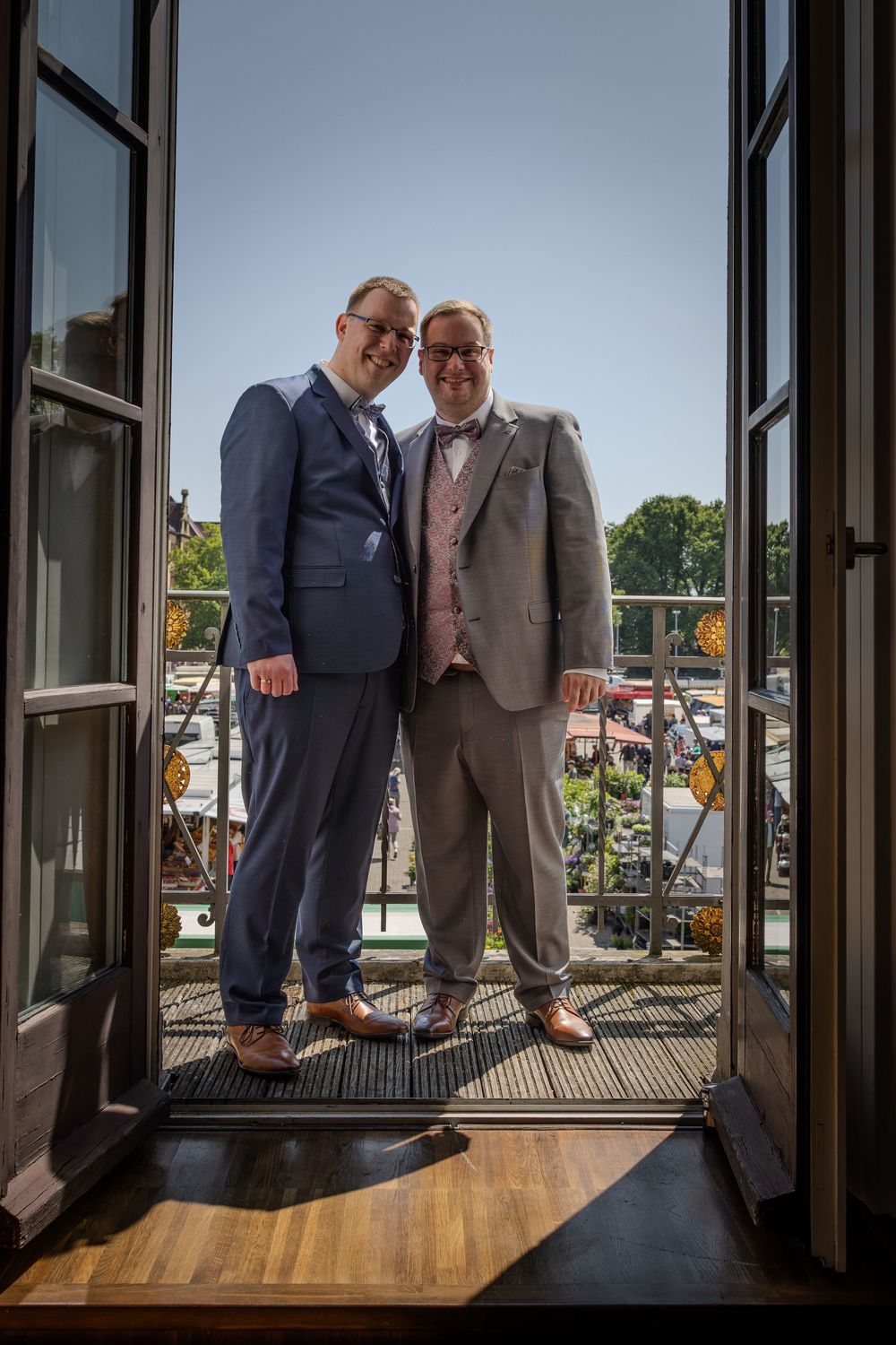 Two people in suits stand together at a window ledge in an office building.