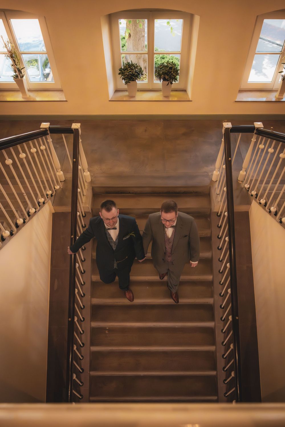 A sequence of photos showing two people descending wooden stairs in a warmly lit interior space.