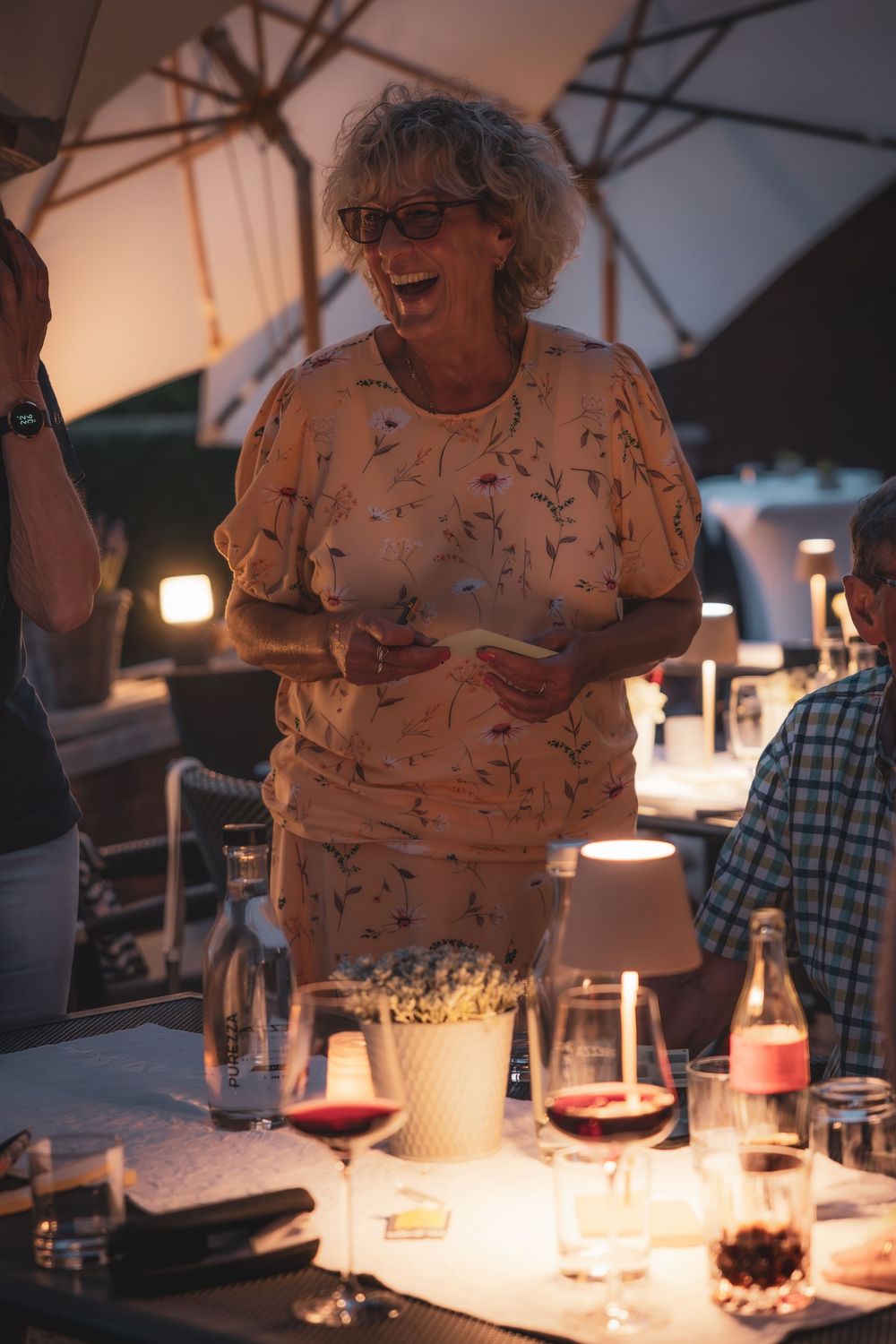 A group of people enjoying wine and conversation at a dimly lit dinner table during an evening gathering.