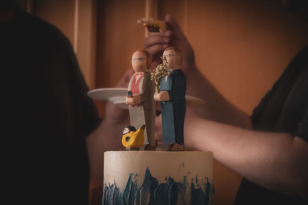 A wedding cake topper featuring small decorative figures against a dark moody background.
