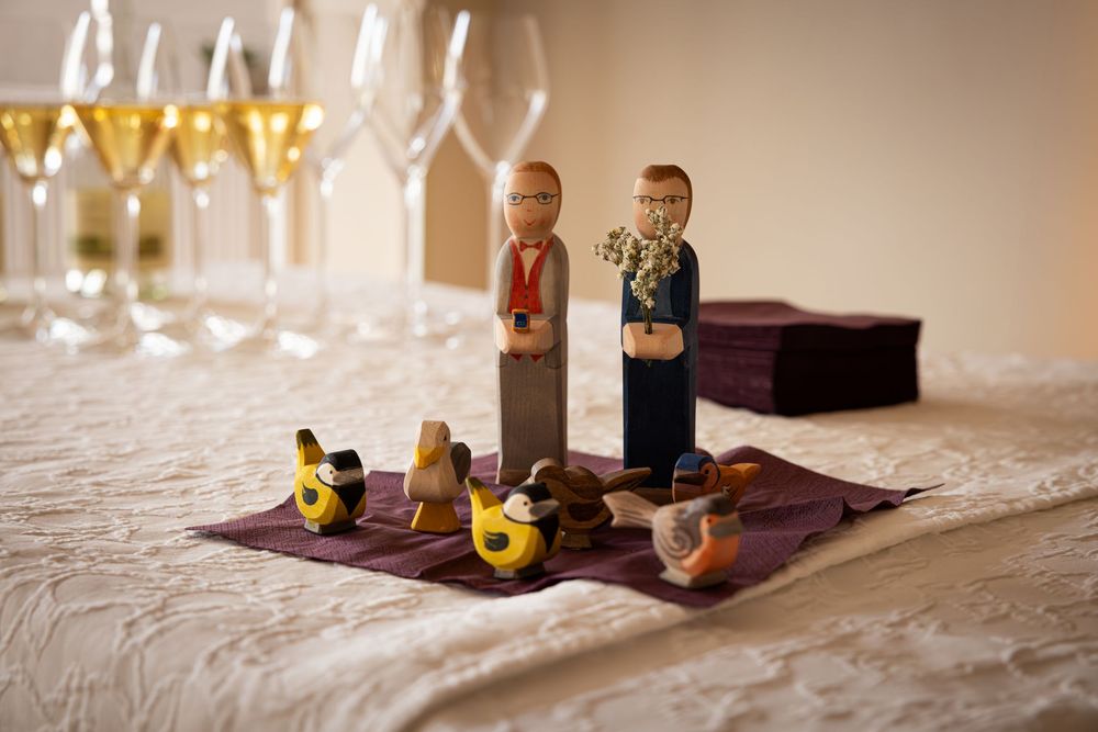 Small wooden LEGO figurines stand beside wine glasses on a white tablecloth in a wedding reception setting.