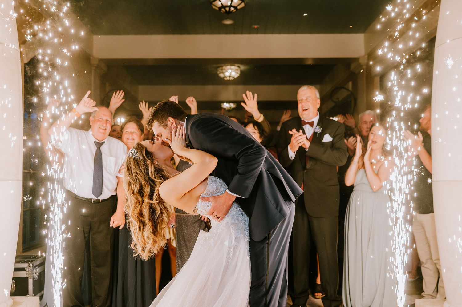 Wedding celebration with sparkler effects and guests dancing in an elegant white venue.