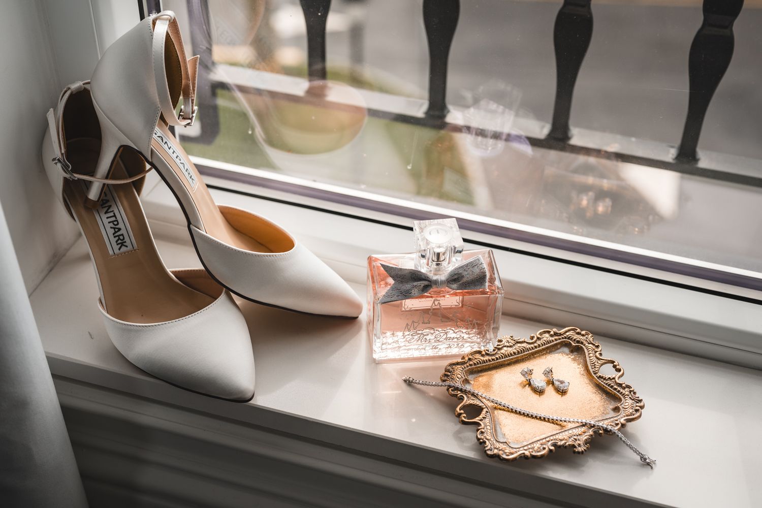 White bridal shoes and perfume bottle arranged on windowsill with elegant accessories.