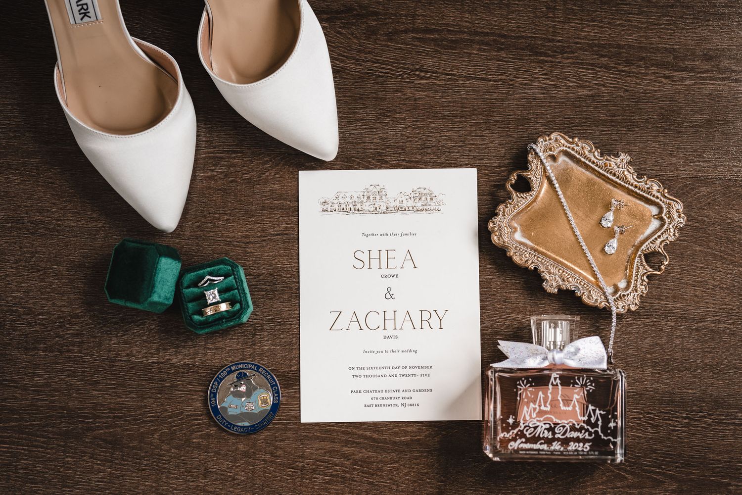 Wedding invitation with white shoes and perfume bottles arranged on dark wooden surface.