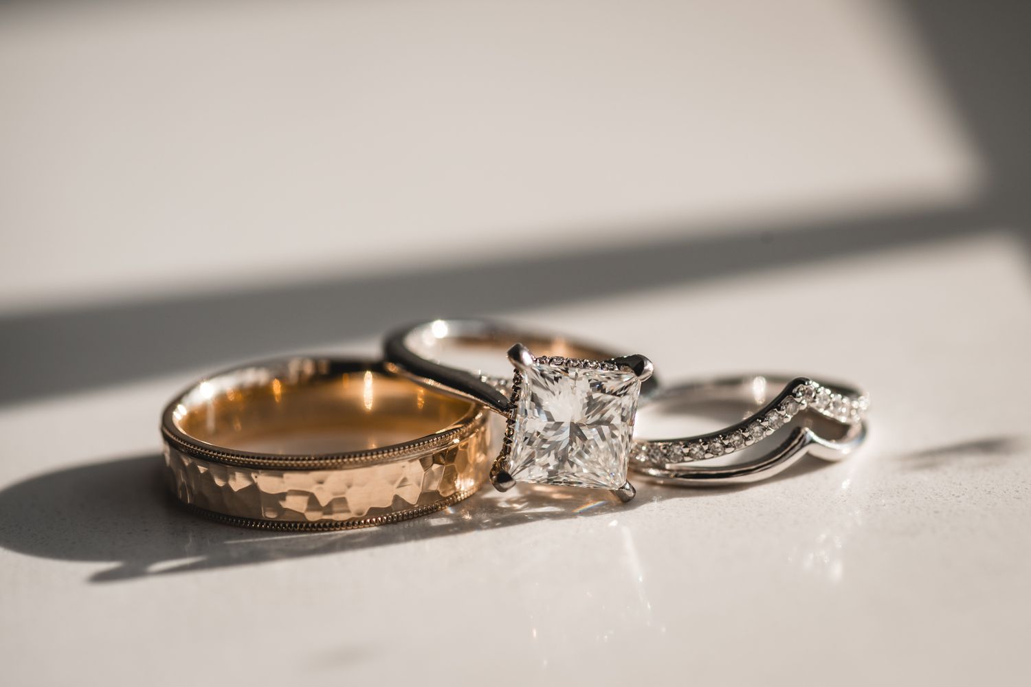 Wedding rings casting dramatic shadows with diamond engagement ring in center focus.