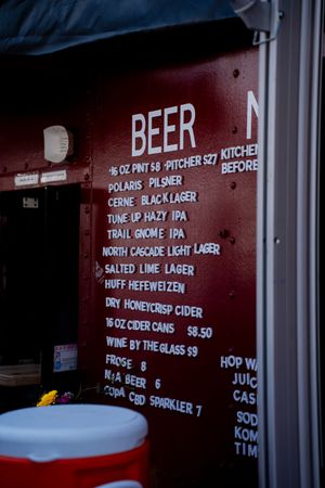 A rustic beer menu board displays craft beer selections including pilsners, lagers and IPAs with prices.