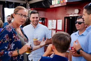 A group of people enjoying drinks and conversation outside a red-painted establishment on a sunny day.