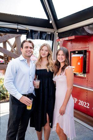 Group of friends enjoying drinks and socializing at an outdoor bar patio on a sunny day.