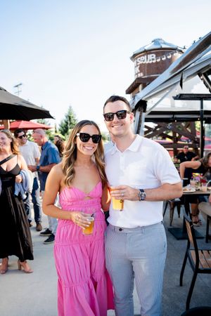 A couple enjoying drinks together at an outdoor venue, with the person in pink and white attire smiling.