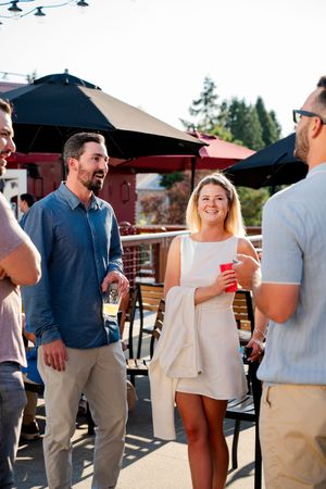 Casual outdoor gathering with people socializing and drinking under patio umbrellas on a sunny day.