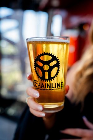 Close-up shots of golden craft beer glasses featuring the Chainline Brewing Company logo and gear emblem.