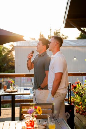 Friends relaxing on a rooftop patio during sunset with colorful flowers and drinks visible.