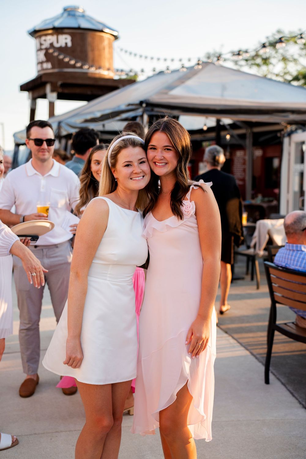 Group of friends in white summer outfits enjoying a casual outdoor event at a brewery patio.