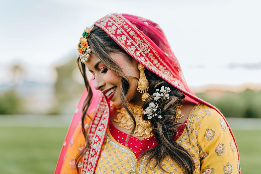 Bride in traditional yellow and red Indian wedding attire with ornate jewelry and henna designs.