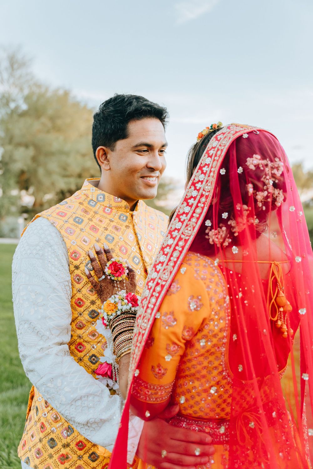 Couple in vibrant orange and red traditional wedding attire share intimate moment outdoors.
