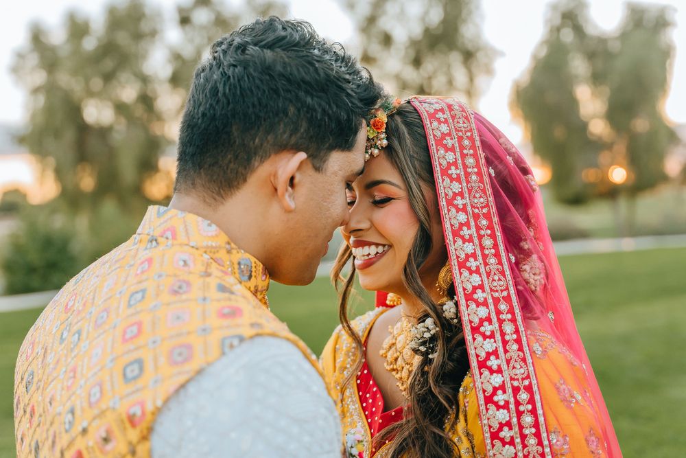 Intimate moment between Indian bride and groom in traditional wedding attire outdoors at sunset.