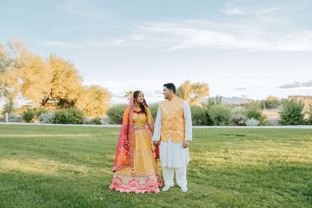 Couple in traditional South Asian wedding attire standing in a garden setting.