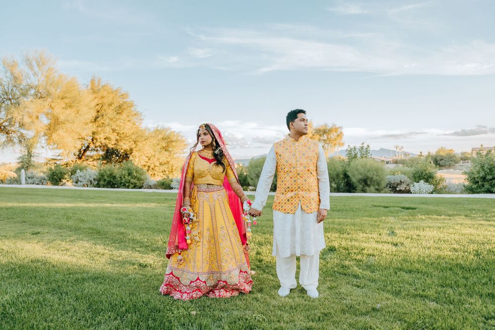 A couple poses in a scenic outdoor setting with fall foliage and green fields in the background.