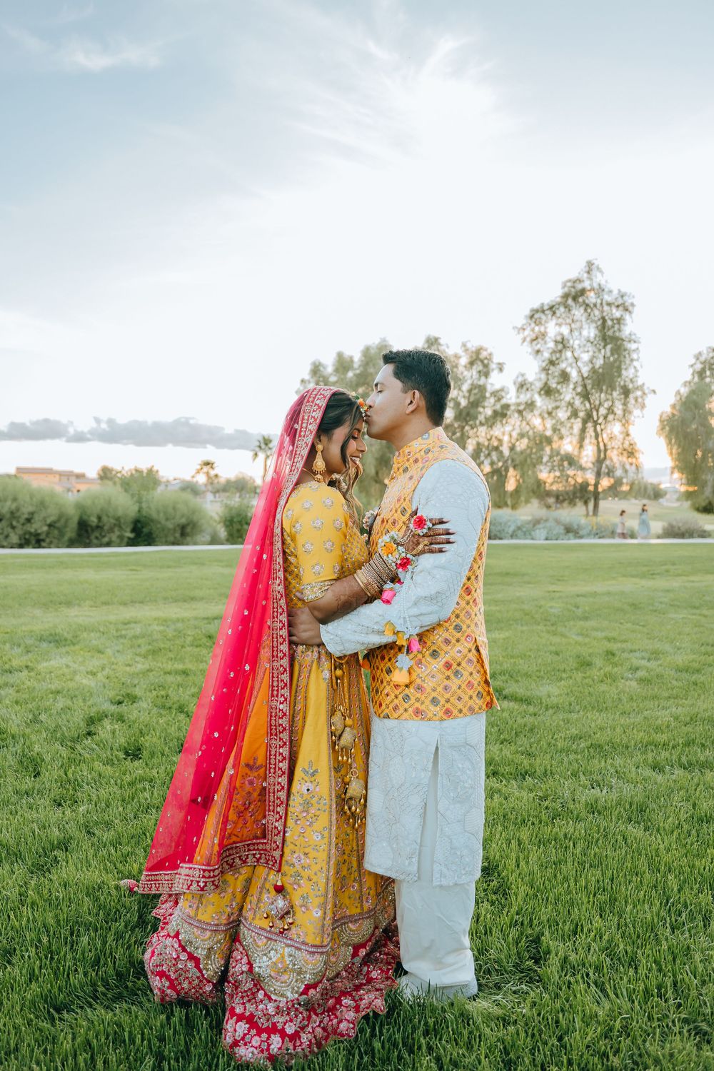 South Asian wedding couple embracing in a scenic outdoor field during golden hour.
