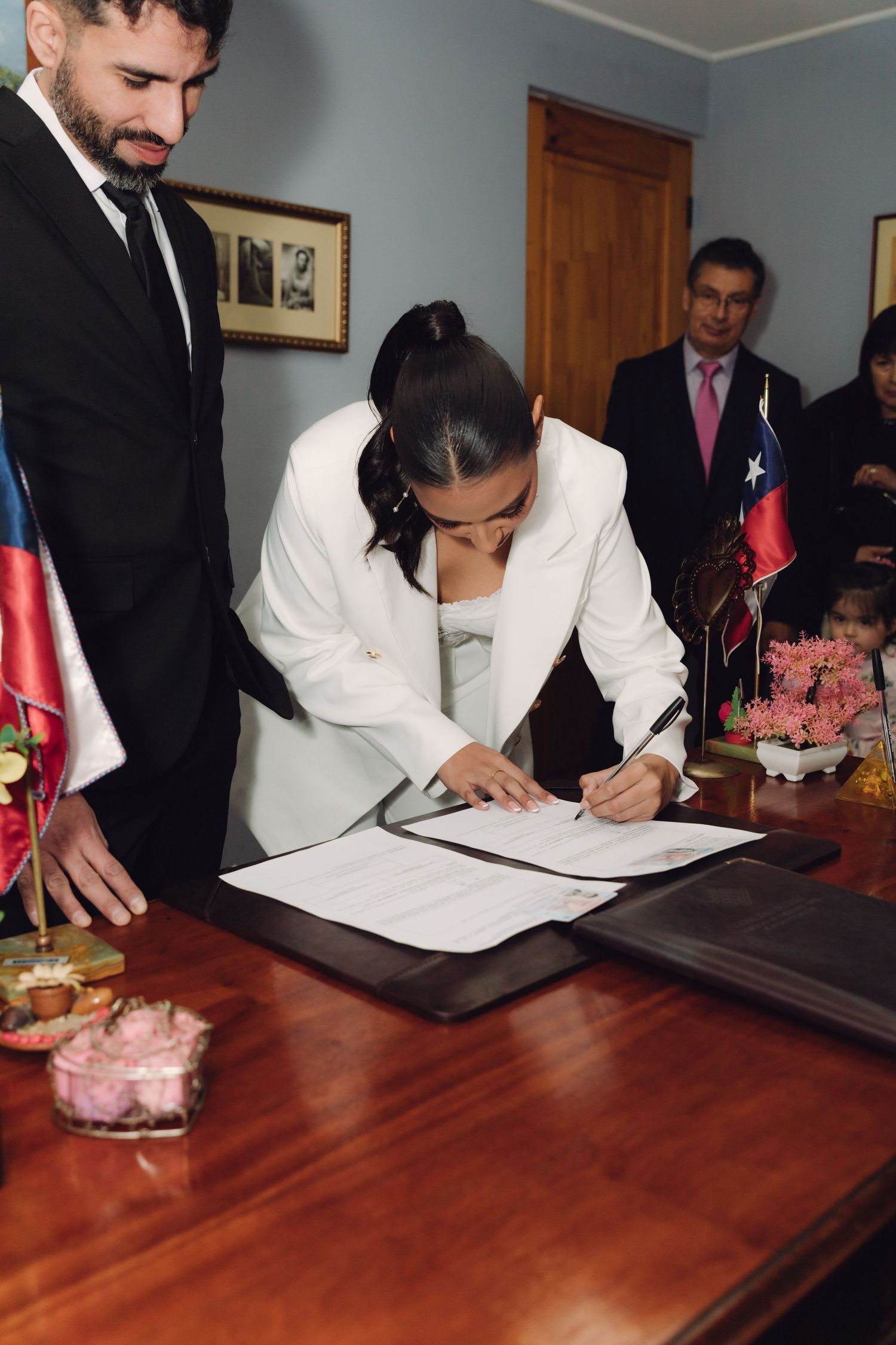Bride in white suit signing wedding documents at civil ceremony registry office in Chile.