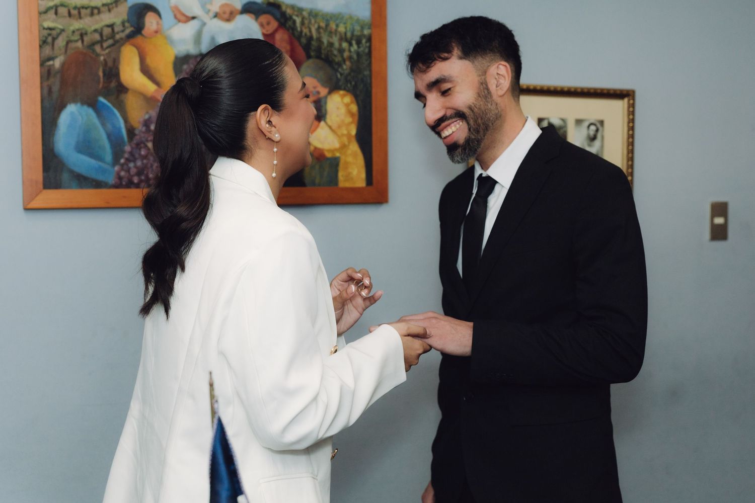 Bride in white suit and groom in black suit exchanging rings at civil wedding.