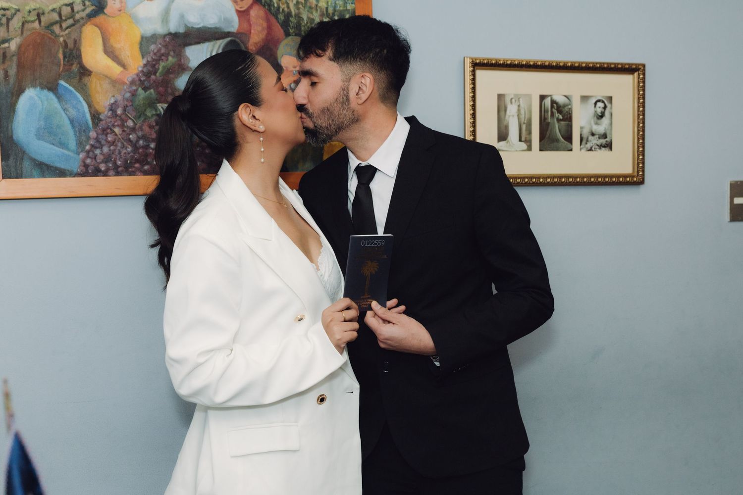 Newlyweds sharing a kiss while holding their marriage certificate after ceremony.