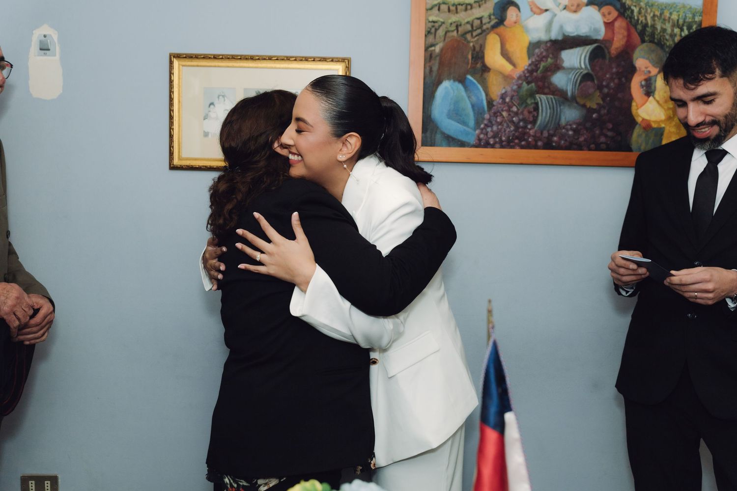 Bride in white suit sharing a warm congratulatory hug with a female guest.