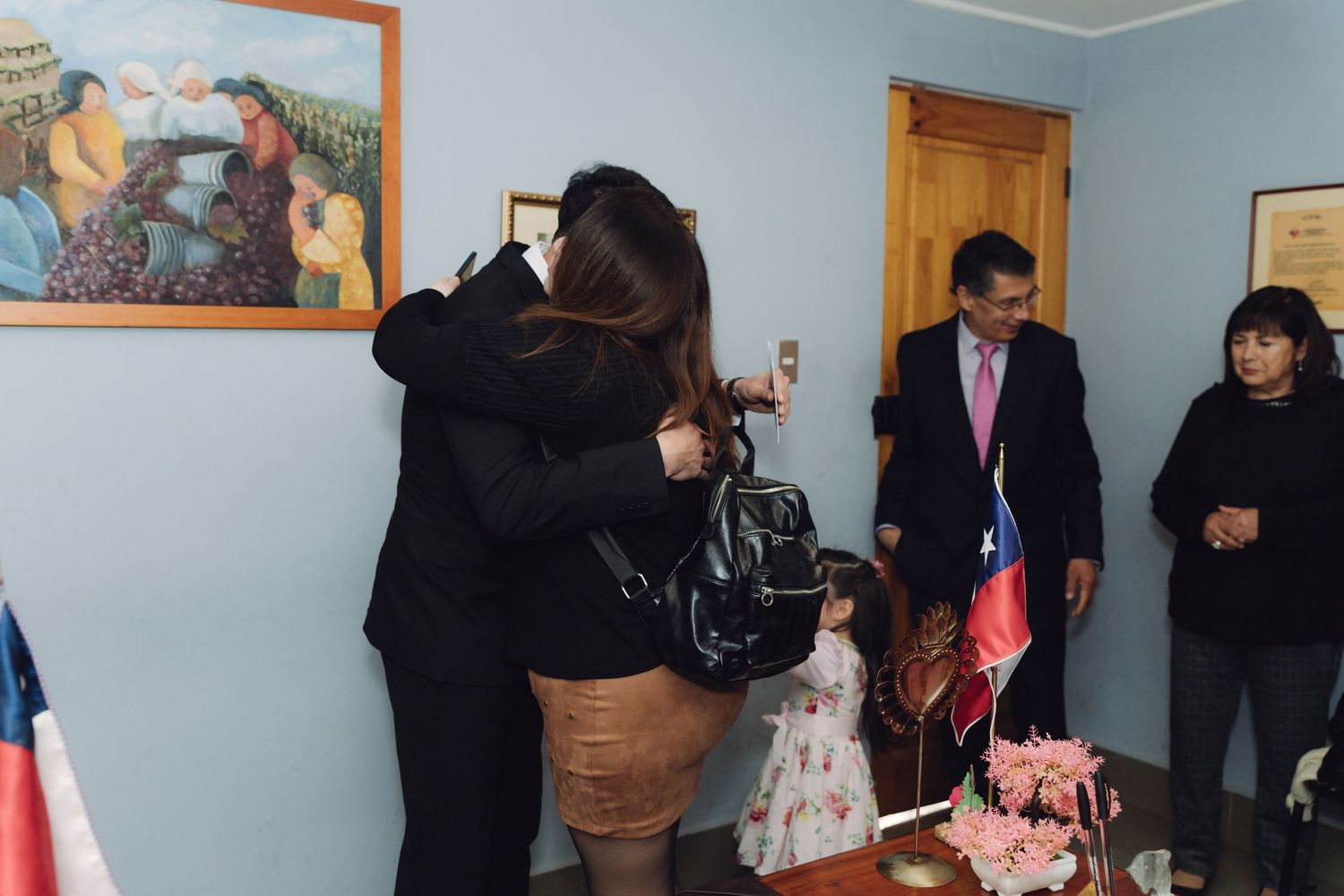 Two women embracing warmly at a Chilean civil ceremony with Chilean flag and floral decorations visible.