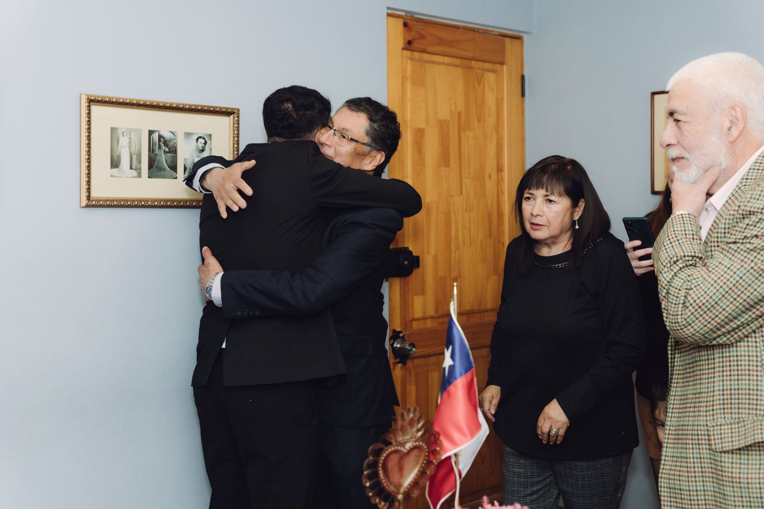Two men sharing a heartfelt hug at a formal Chilean civil ceremony while guests look on smiling.