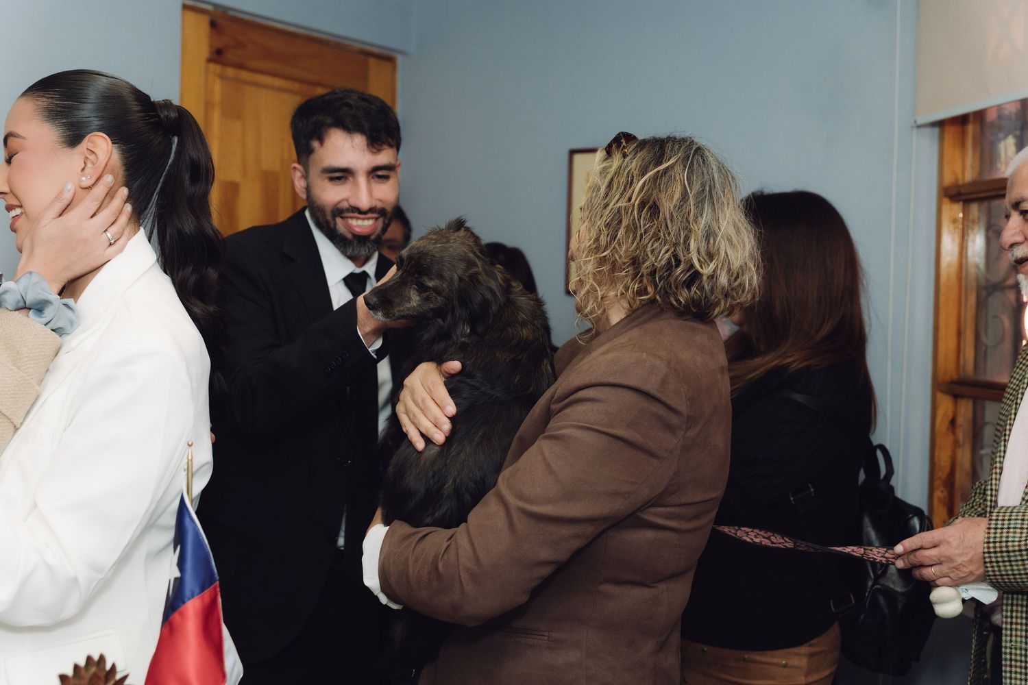 Smiling man in suit holding a fluffy dog at a cheerful Chilean civil ceremony gathering.