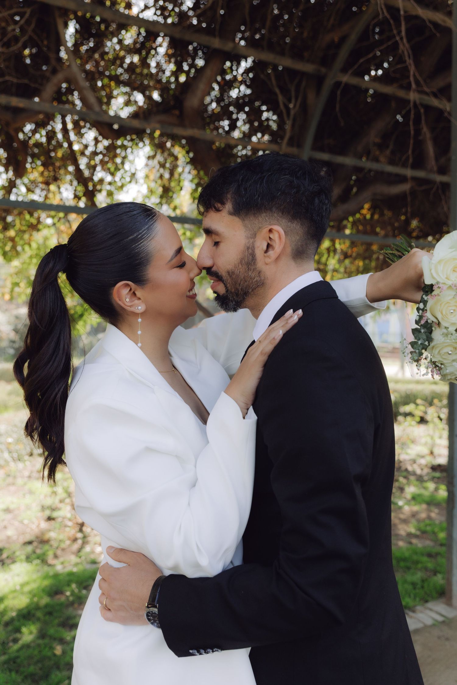 Bride and groom sharing a kiss under garden pergola on wedding day.