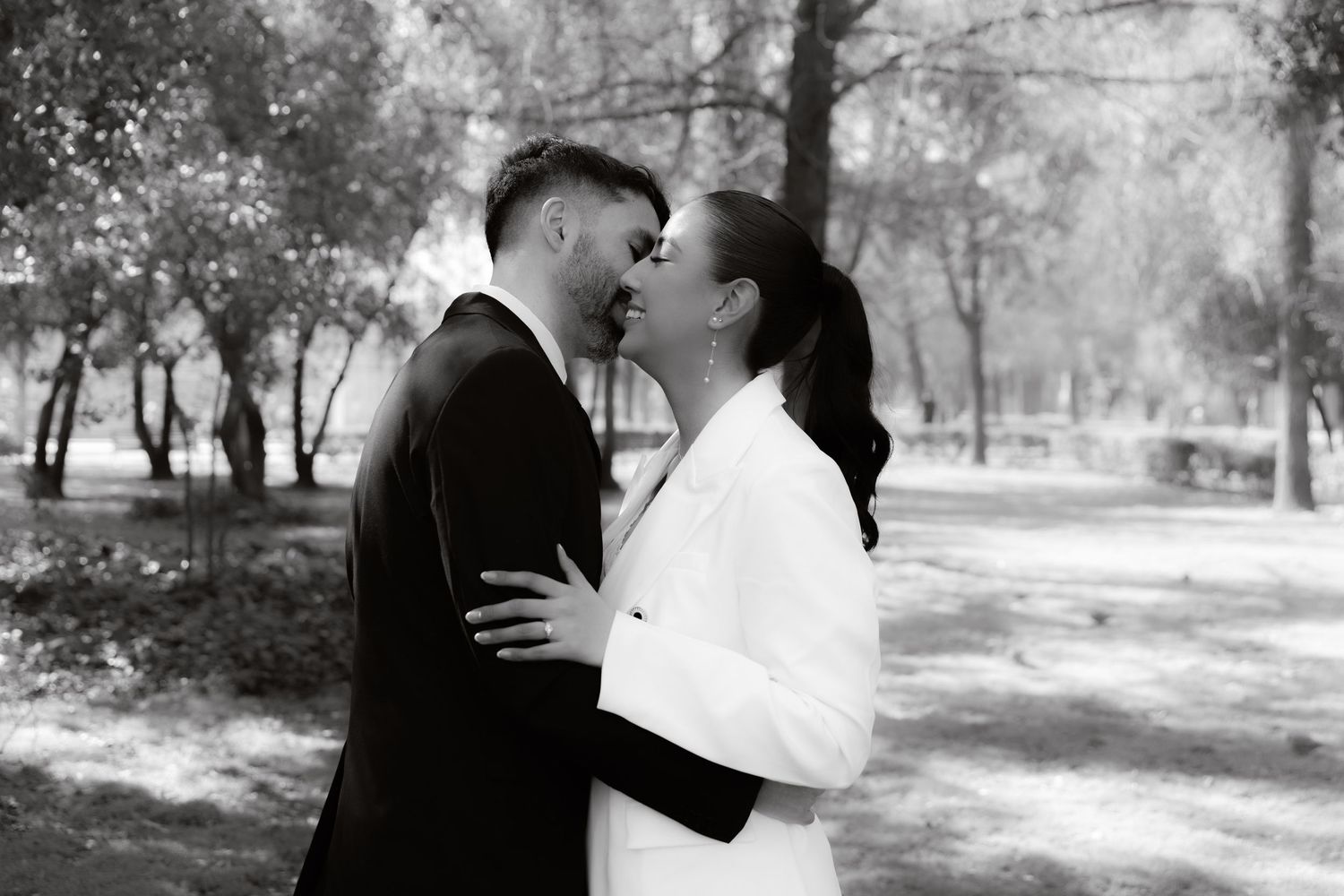 Black and white wedding portrait of couple almost kissing while embracing in a lush outdoor park.