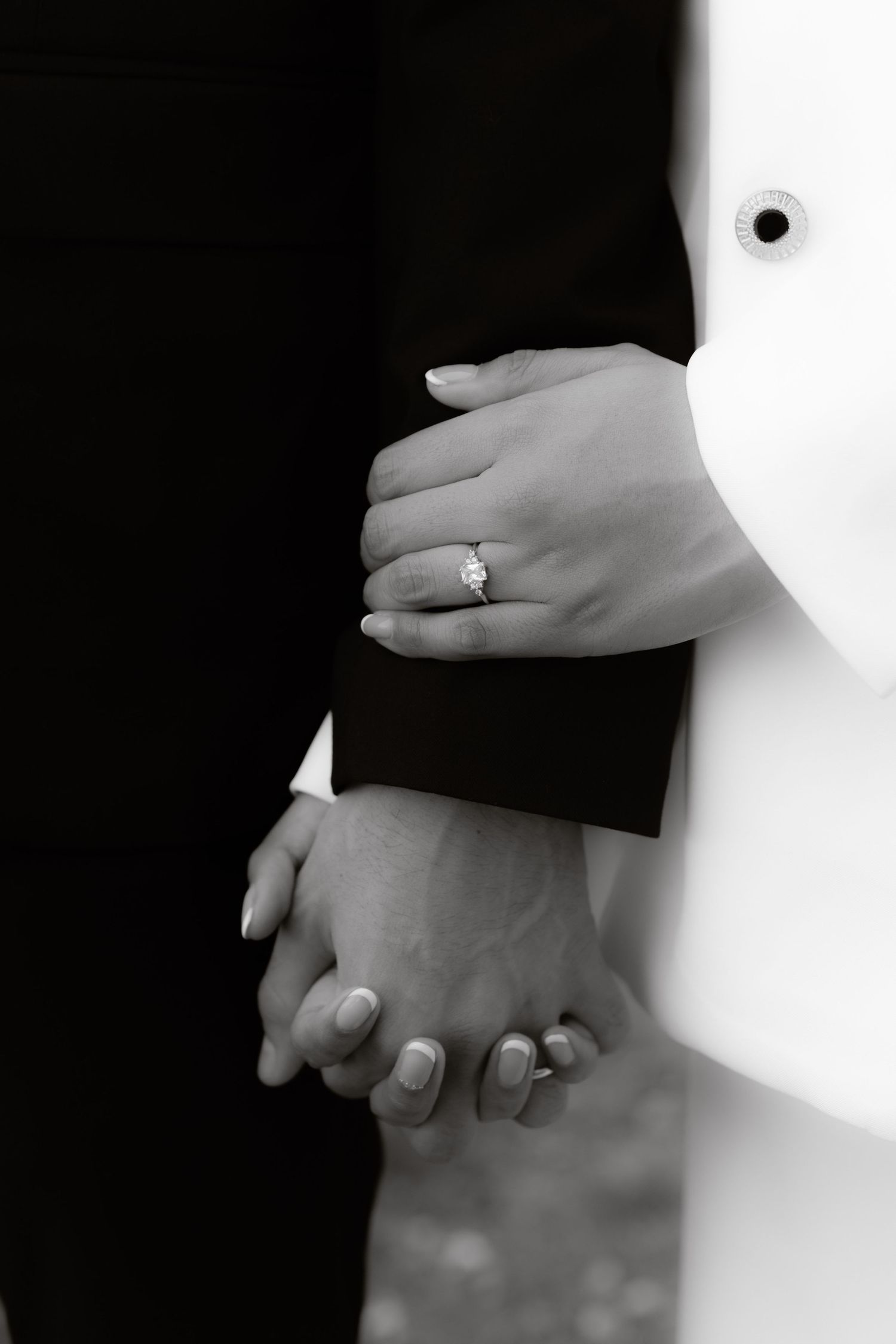 Black and white detail shot of newlyweds holding hands with bride wearing a sparkling diamond ring.