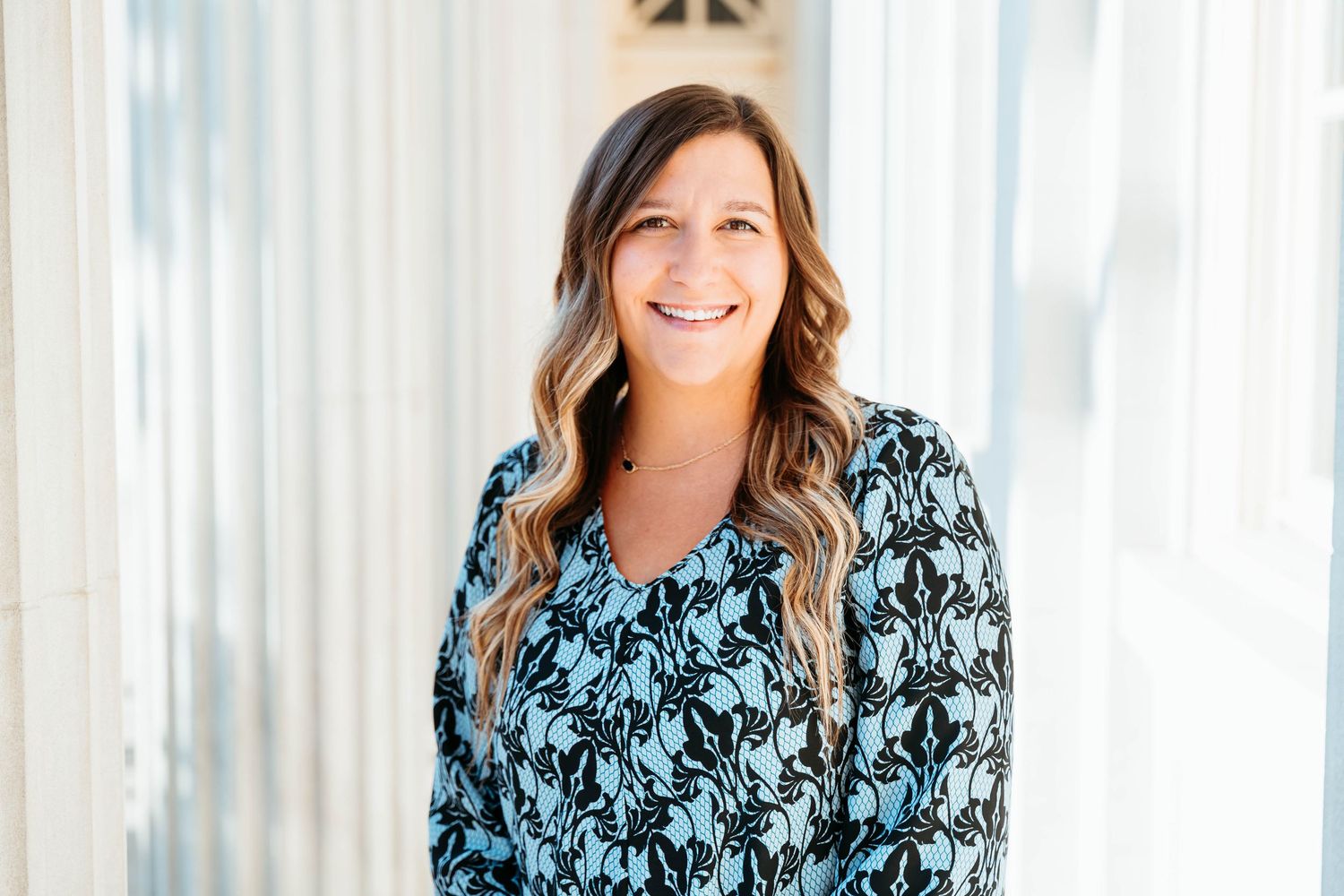 Professional headshot of someone wearing a blue floral print top against a light colored background.