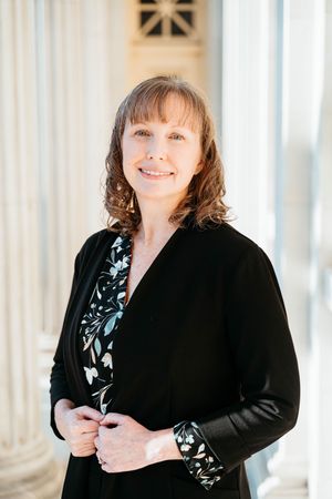 Professional portrait series showing a figure in a black cardigan and floral top against a bright columned backdrop.