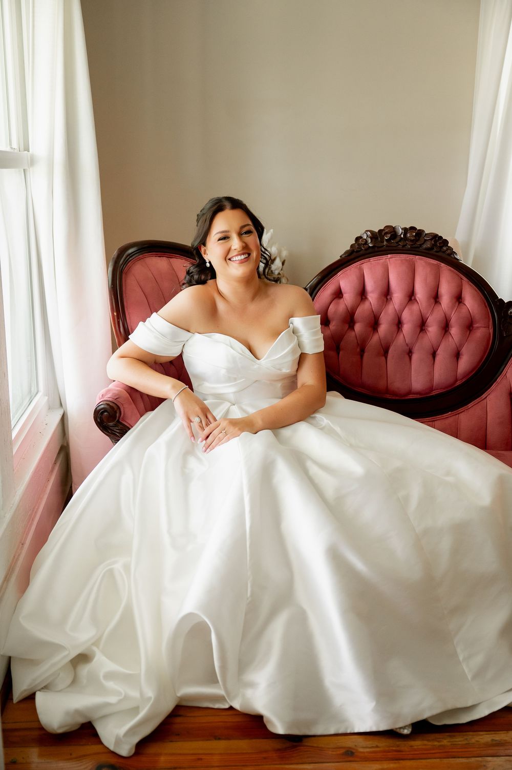 Candid bridal portraits on pink tufted sofa showing joyful moments in white wedding dress.