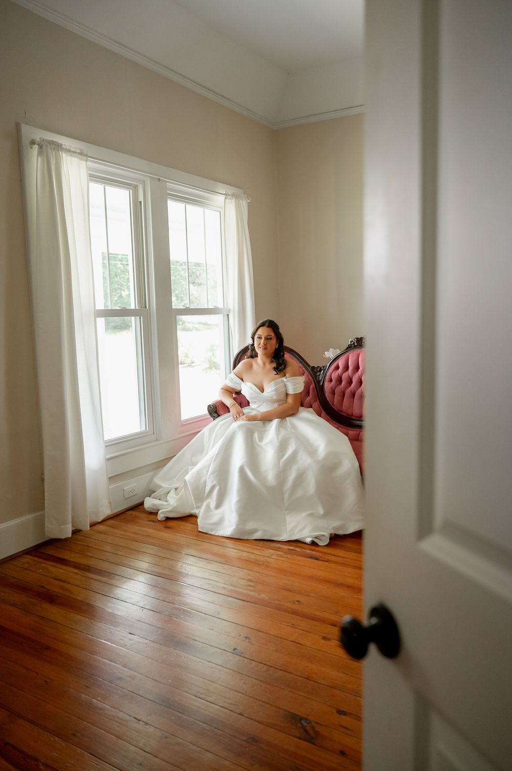 Artistic wide angle view of bridal portraits on vintage pink sofa in bright room.