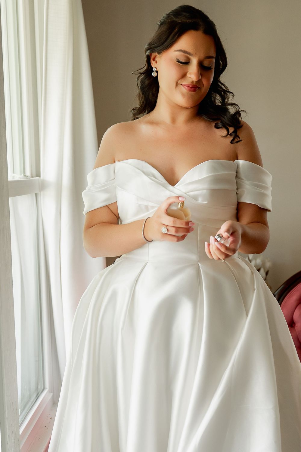 Elegant off-shoulder white wedding dress details captured in natural window light.