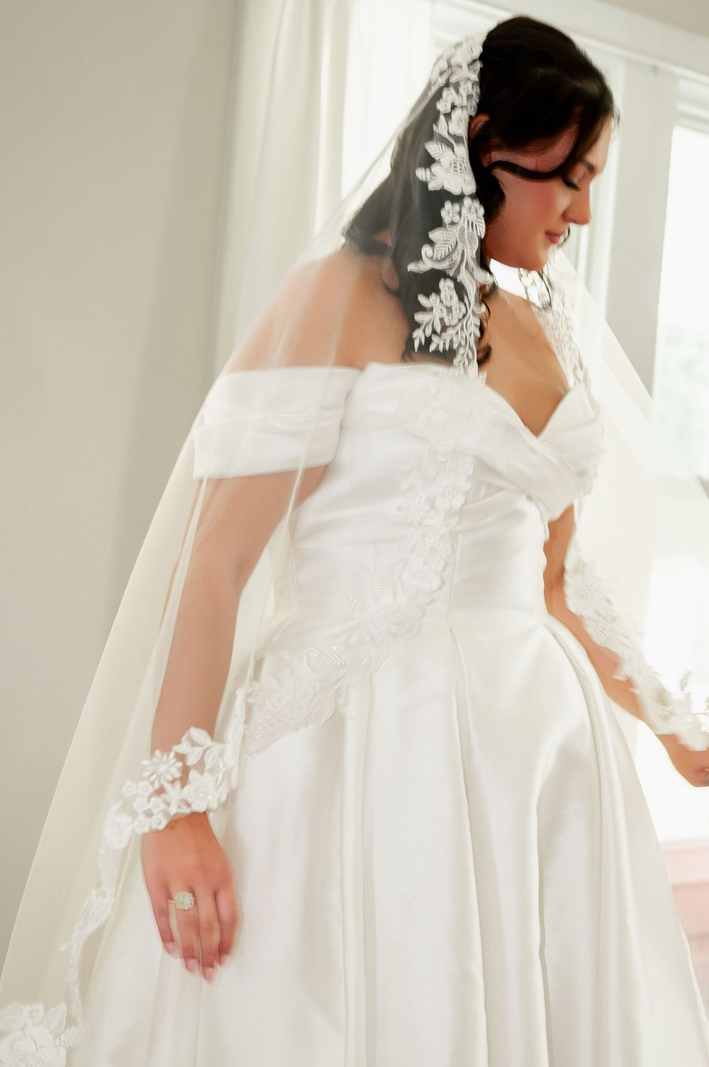 Delicate details of off-shoulder wedding dress and veil captured in soft natural light.
